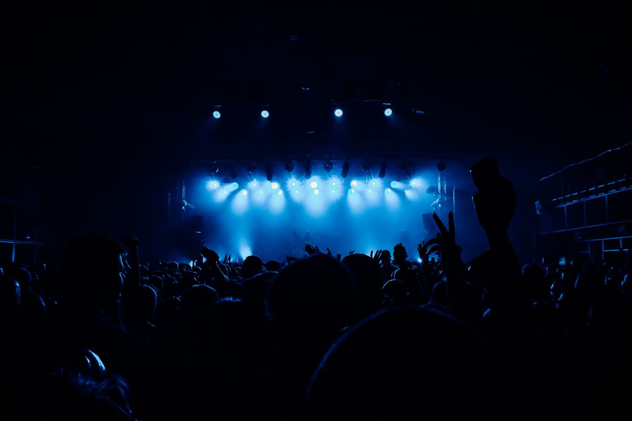 the-story A vibrant concert scene with a lively crowd and dramatic blue stage lighting.